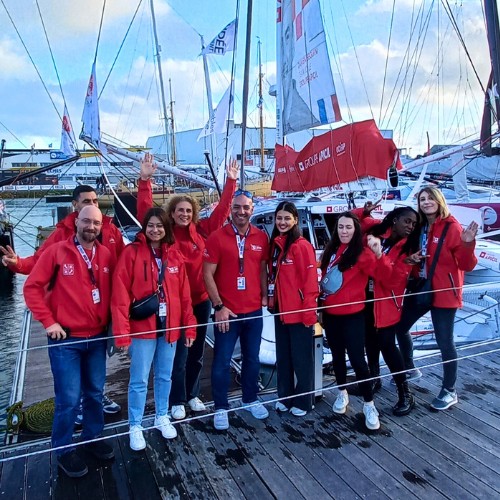 Des collaborateurs Apicil aux cotés de Damien Seguin navigateur handisport participant au Vendée Globe devant le bateau sponsorisé par Apicil.